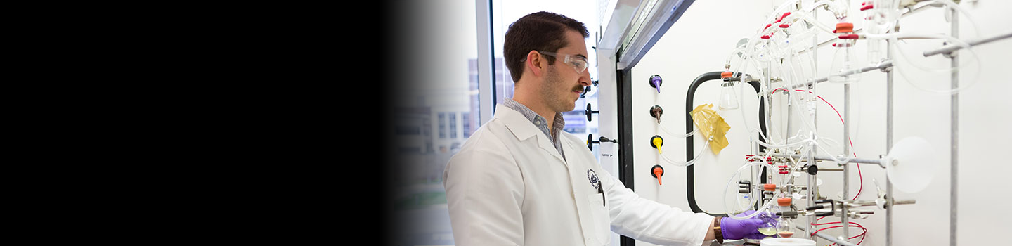 Scientist wearing goggles turning on machine in a lab.